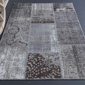 Op de afbeelding: Een grijs en bruin patchwork tapijt met een verweerde look. Het tapijt is gemaakt van verschillende stukken stof die aan elkaar zijn genaaid.