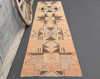 May include: A long, narrow rug with a geometric pattern in shades of brown, beige, and cream. The rug has a traditional, tribal design with repeating star shapes and diamond patterns.