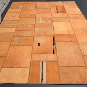 Puede incluir: Una alfombra de patchwork hecha de varios tonos de tela marrón y beige. La alfombra está compuesta por muchos cuadrados y rectángulos diferentes, cada uno con un patrón o textura diferente. La alfombra es una excelente manera de agregar un toque de encanto rústico a cualquier habitación.