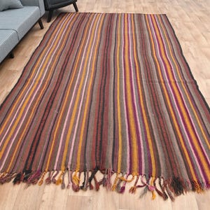 May include: A long, narrow striped rug with a fringe on both ends. The rug is made of wool and has a variety of colors, including brown, orange, pink, and purple.