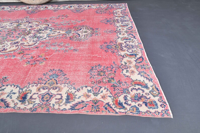 K&ouml;nnte beinhalten: Ein vintagefarbener rosa Teppich mit einem floralen Muster in Blaut&ouml;nen, Wei&szlig; und Rosa. Der Teppich hat einen abgenutzten Look und ist perfekt, um jedem Raum einen Hauch von Boho-Stil zu verleihen.