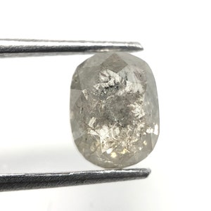 May include: A faceted, oval-shaped, gray diamond held by metal tweezers. The diamond has internal inclusions and a polished surface, reflecting light. The gemstone is set against a white background.