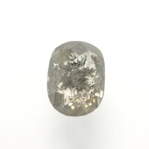 May include: A faceted, oval-shaped, salt and pepper diamond. The gemstone has a gray hue with dark inclusions and a brilliant, reflective surface. The diamond is set against a white background.