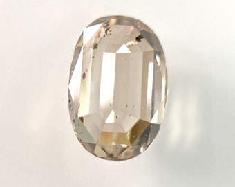 May include: An oval-cut, faceted gemstone with a light brown hue. The gem has a polished surface with multiple facets, reflecting light. The gemstone is set against a white background, highlighting its clarity and color. This gemstone is suitable for jewelry.