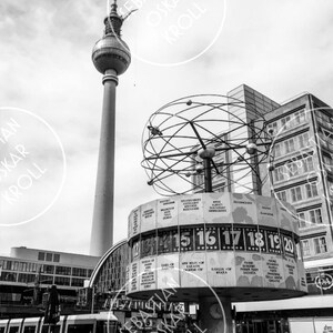 Peut inclure: Une photo en noir et blanc de l'horloge mondiale de Berlin, une grande structure circulaire avec un globe rotatif et un cadran d'horloge affichant l'heure dans différentes villes du monde. La tour de télévision de Berlin est visible en arrière-plan.