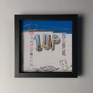 K&ouml;nnte beinhalten: Gerahmtes Kunstwerk mit dem Wort "1UP" in metallischen Ballonbuchstaben auf einer wei&szlig;en Wand. Der Hintergrund zeigt einen blauen Himmel, einen Baukran und Graffiti. Das Kunstwerk befindet sich in einem schwarzen Rahmen.