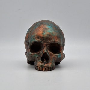 May include: A small, detailed skull sculpture with a copper and turquoise paint finish.