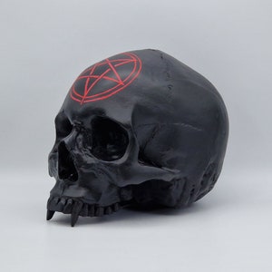 May include: Black skull sculpture with a red pentagram painted on the forehead.