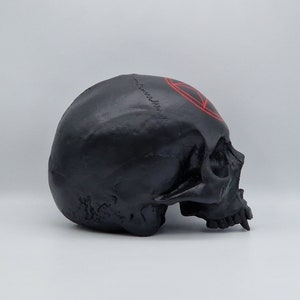May include: Black skull with a red pentagram painted on the forehead. The skull is made of resin and is a decorative object.