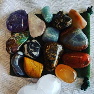 May include: A collection of 14 polished stones in various colors and patterns, including green, brown, blue, white, gray, red, orange, and purple. The stones are arranged on a green felt surface.