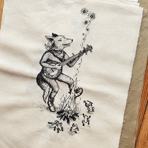 May include: A black and white illustration of a fox playing a banjo in front of a campfire with four frogs around it. The fox is wearing a bandana and has a bushy tail. The banjo has a round body and five strings. The campfire is made of flames and logs. The frogs are sitting on the ground and have big eyes.