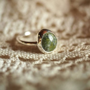 May include: A silver ring with a green and white oval gemstone set in a bezel setting.