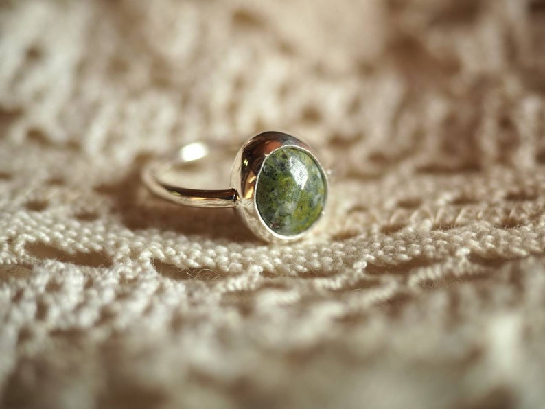 May include: A silver ring with a green and white oval gemstone set in a bezel setting.