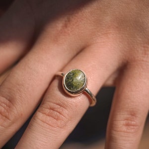 May include: A silver ring with a green and white oval-shaped stone set in a bezel setting.