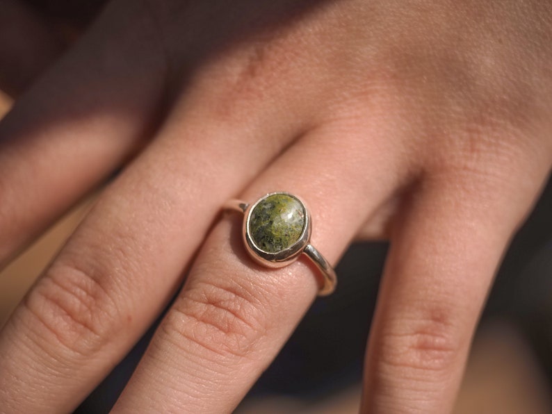 May include: A silver ring with a green and white oval-shaped stone set in a bezel setting.