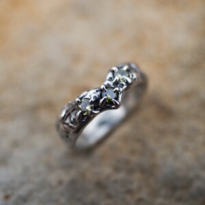 May include: A silver ring with a unique, organic design featuring three green gemstones.