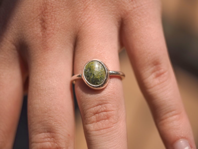 May include: A silver ring with a green oval-shaped gemstone set in a bezel setting.