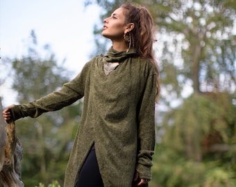 May include: An olive green tunic sweater with a high collar and a split front. The sweater is paired with black leggings and brown boots. The model is standing outdoors near a tree.