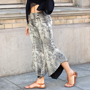 Puede incluir: Una mujer con un top negro corto de manga larga y una falda estampada en blanco y negro. Lleva sandalias marrones y está de pie frente a una pared de ladrillo.