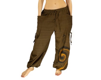 Puede incluir: Una mujer con pantalones marrones holgados con un diseño decorativo en la pierna derecha. Los pantalones tienen cintura con cordón y bolsillos a los lados.