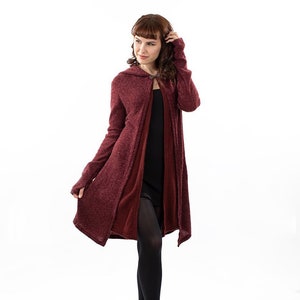 Op de afbeelding: Een lange, bordeauxrode capuchontrui met een losse pasvorm en een licht asymmetrische zoom. De trui is gemaakt van een zachte, textuurrijke stof.