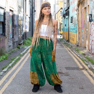 Puede incluir: Pantalones harén verdes y dorados estampados con bolsillos. Los pantalones tienen un corte amplio y holgado y están hechos de una tela ligera. Los pantalones se combinan con un top corto blanco y zapatillas negras. Los pantalones presentan un diseño circular.