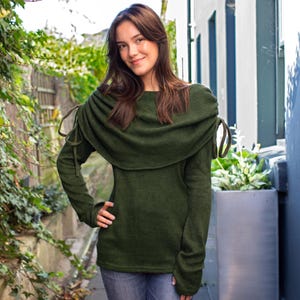 Peut inclure: Un pull vert foncé avec un col roulé unique et des manches longues. Le pull présente des détails de liens aux épaules. Le modèle porte un jean bleu. Le pull est fait d'une matière douce et confortable.