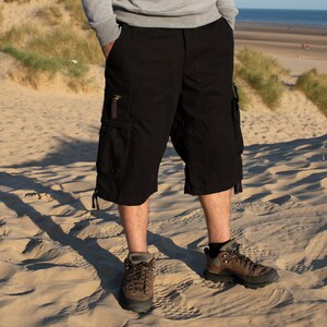 May include: A pair of black cargo shorts with multiple pockets and a drawstring at the bottom. The shorts are worn by a person standing on a sandy beach.