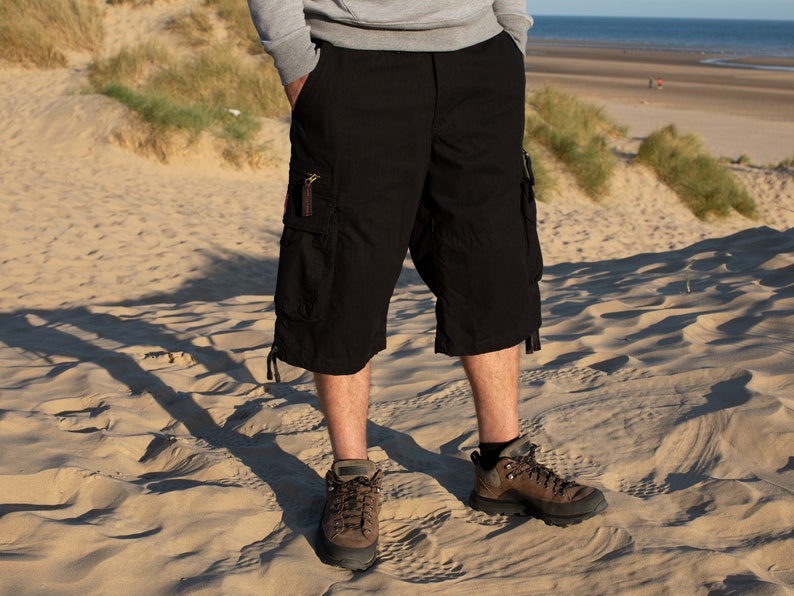 May include: A pair of black cargo shorts with multiple pockets and a drawstring at the bottom. The shorts are worn by a person standing on a sandy beach.