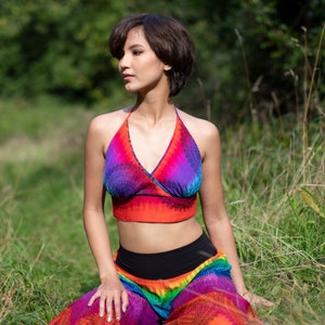 Könnte beinhalten: Eine Frau trägt ein farbenfrohes Halstuch und einen Regenbogenrock. Das Oberteil ist ein leuchtend orangefarbenes, violettes und blaues Batik-Muster. Der Rock ist eine Mischung aus Rot, Orange, Gelb, Grün, Blau und Lila.