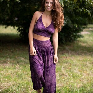 May include: A woman wearing a purple crop top and matching pants with a paisley print. The outfit is made of a soft, flowing fabric.