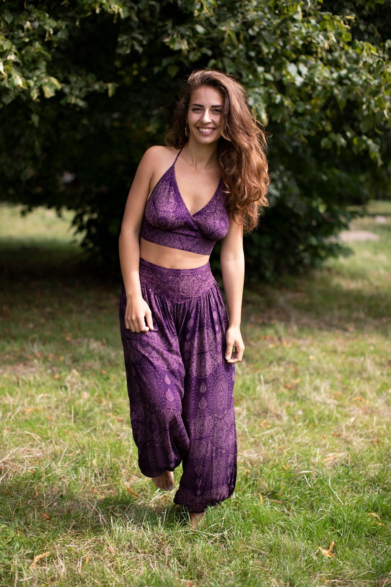 May include: A woman wearing a purple crop top and matching pants with a paisley print. The outfit is made of a soft, flowing fabric.