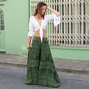 Può includere: Una donna indossa un top bianco corto con laccetti e pantaloni larghi con stampa verde.