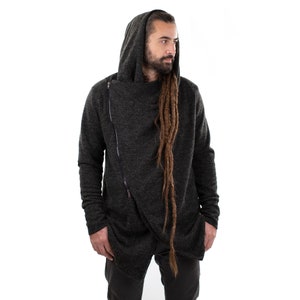 May include: Dark gray hooded sweater with an asymmetrical zipper closure. The long-sleeved sweater has a draped design and a hood. The sweater is made of a soft, textured material. The model is wearing dark pants.