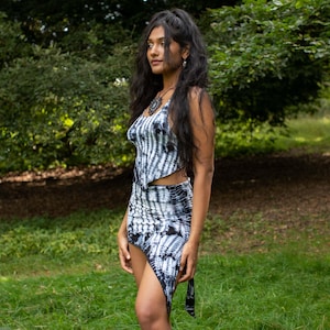 Puede incluir: Una mujer con un top y una falda de color negro y blanco con estampado tie-dye. La falda es asimétrica y tiene un lazo largo en un lado.