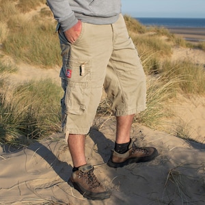 May include: A person wearing beige cargo shorts and brown hiking boots standing on a sandy dune.