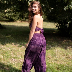 May include: A woman wearing a purple halter top and matching printed pants. The pants are loose-fitting and have a wide leg.