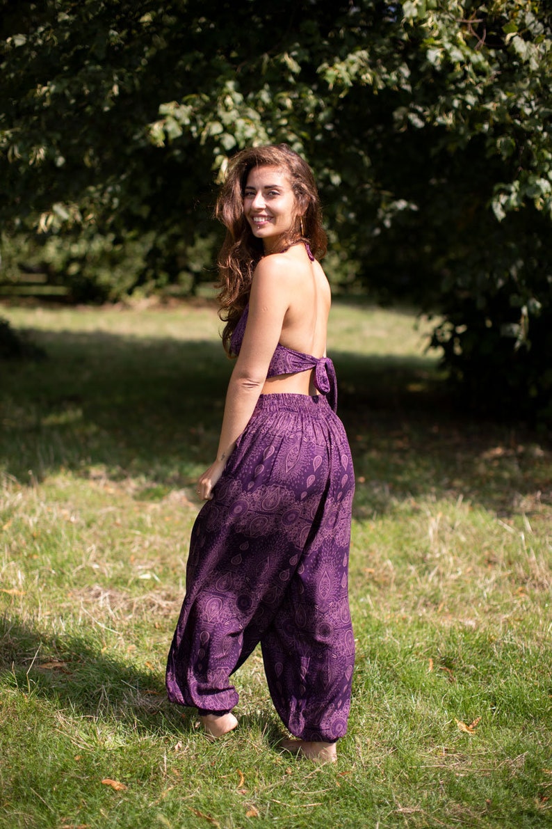 May include: A woman wearing a purple halter top and matching printed pants. The pants are loose-fitting and have a wide leg.