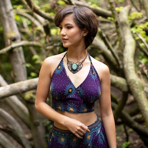 Könnte beinhalten: Eine Frau trägt ein lila-blaues Crop-Top mit Blumenmuster und einen passenden Rock. Sie trägt eine Halskette mit einem großen grünen Steinanhänger.