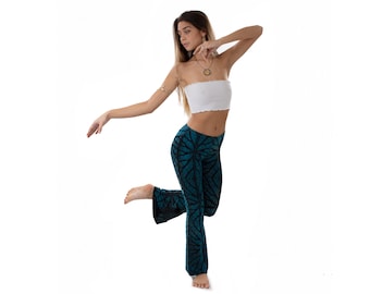 May include: A woman wearing a white tube top and teal blue bell bottom pants with a black and teal pattern. She is standing on one leg with her other leg bent at the knee.
