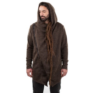 May include: A brown hooded jacket with a diagonal zipper closure. The jacket has long sleeves and a draped front. The model is wearing the jacket over a green shirt and black pants. The jacket is made of a textured fabric.