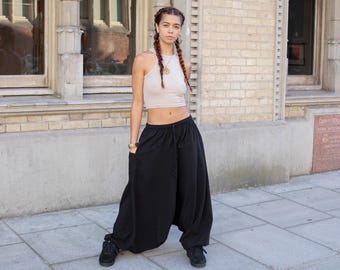 May include: A woman wearing a black, loose-fitting, wide-leg pants with a drawstring waist and a light beige tank top. She is standing in front of a brick wall.