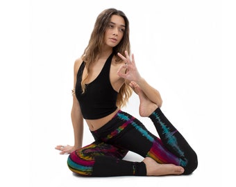 May include: A woman wearing black yoga pants with a colorful tie-dye pattern and a black halter top. She is sitting in a yoga pose with her leg bent behind her and her foot resting on her thigh.