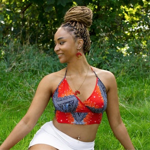 Könnte beinhalten: Ein rotes, weißes und blau gemustertes Neckholder-Top mit passenden Ohrringen und Halskette. Der Schmuck hat ein kreisförmiges Design mit roten Akzenten. Die Frau trägt einen weißen Rock und hat ihr Haar geflochten.
