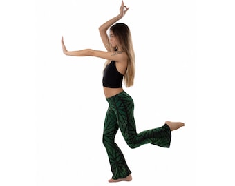 May include: A woman wearing a black crop top and green printed pants with a wide leg. She is posing with her arms raised and one leg extended.