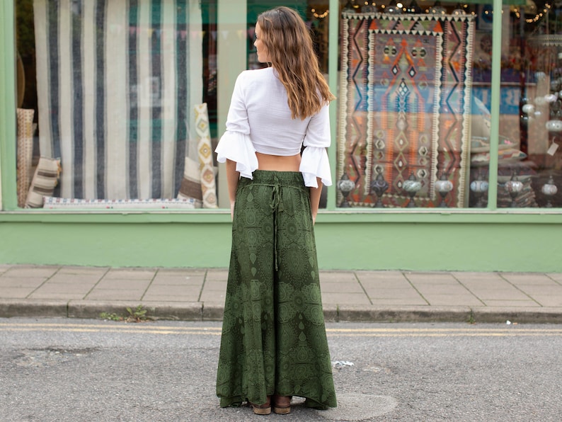 May include: A woman wearing a white crop top with a ruffled neckline and a pair of green printed wide-leg pants.