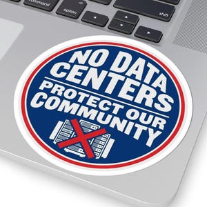 May include: A round sticker with the text "NO DATA CENTERS PROTECT OUR COMMUNITY" in white letters on a blue background, with a red X over a server graphic. The sticker is on a laptop.
