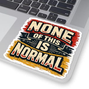 May include: A rectangular sticker with the text "NONE OF THIS IS NORMAL" in a distressed, vintage style. The text is in white, red, black, and yellow, with a grunge effect. The sticker is on a laptop.