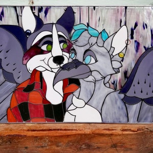 May include: Stained glass panel featuring two anthropomorphic characters. One is a raccoon in a red and black plaid shirt, the other is a bird-like creature. The artwork uses shades of purple, gray, red, and white, with green and blue accents.
