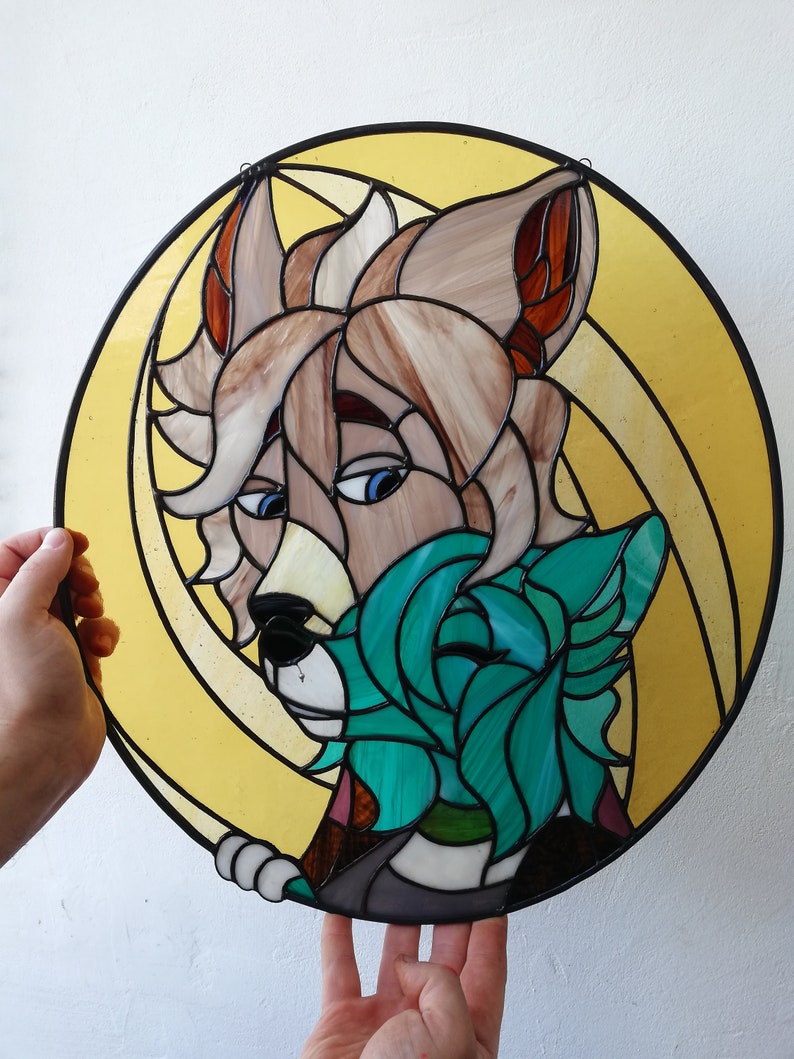 May include: A round stained glass art piece featuring a stylized anthropomorphic wolf with tan and brown fur, blue eyes, and a teal-colored wolf. The artwork is set against a yellow background with black outlines.